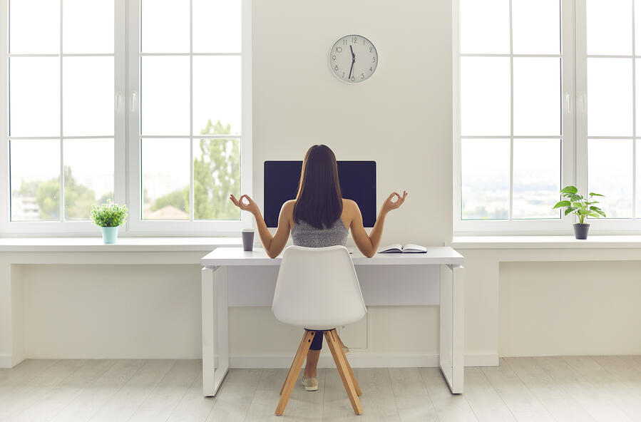 Employee working from home sitting and meditating in front of her computer.
